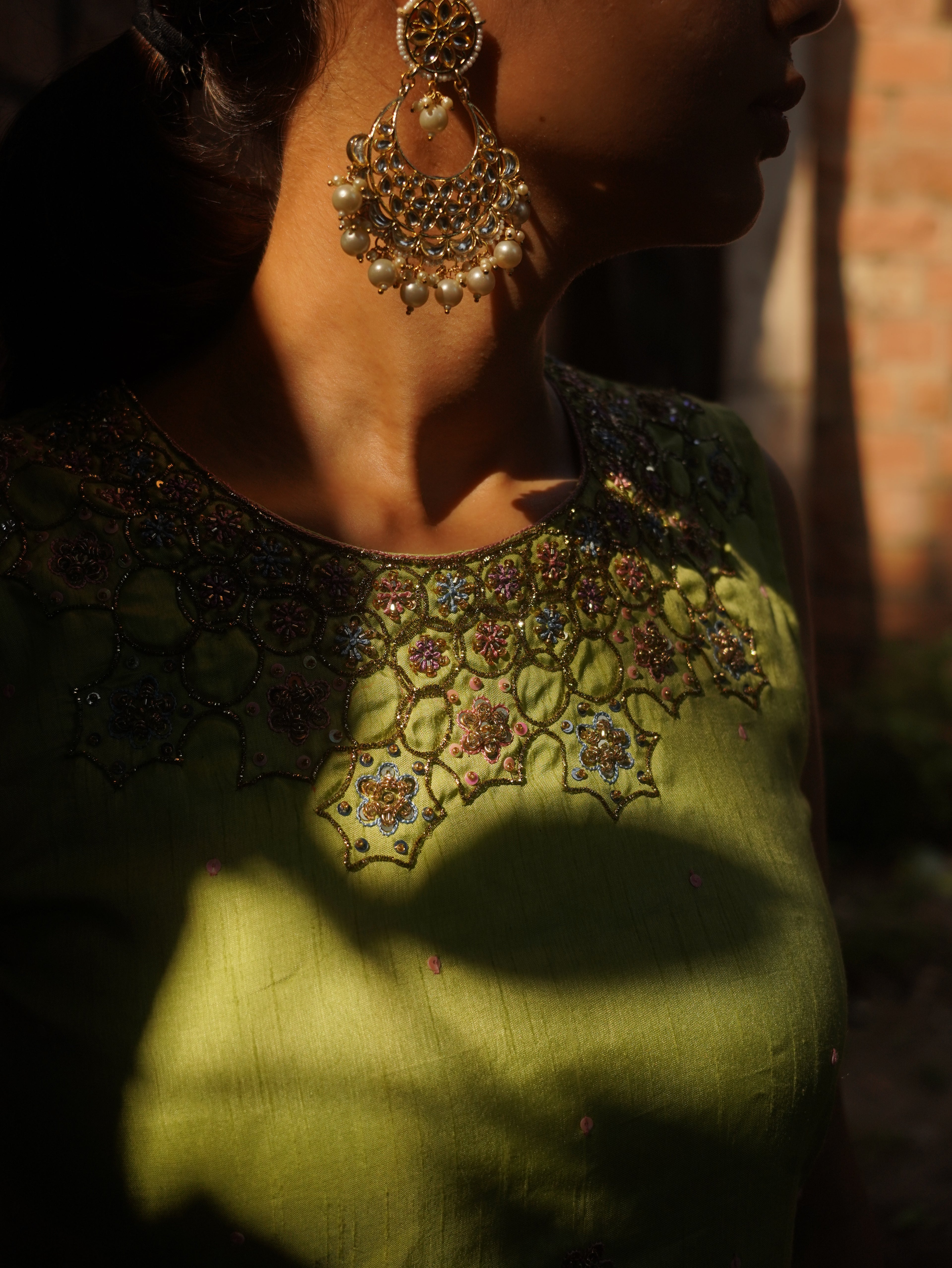 Close-up of a person wearing a green embroidered garment with intricate patterns and gold jewelry.